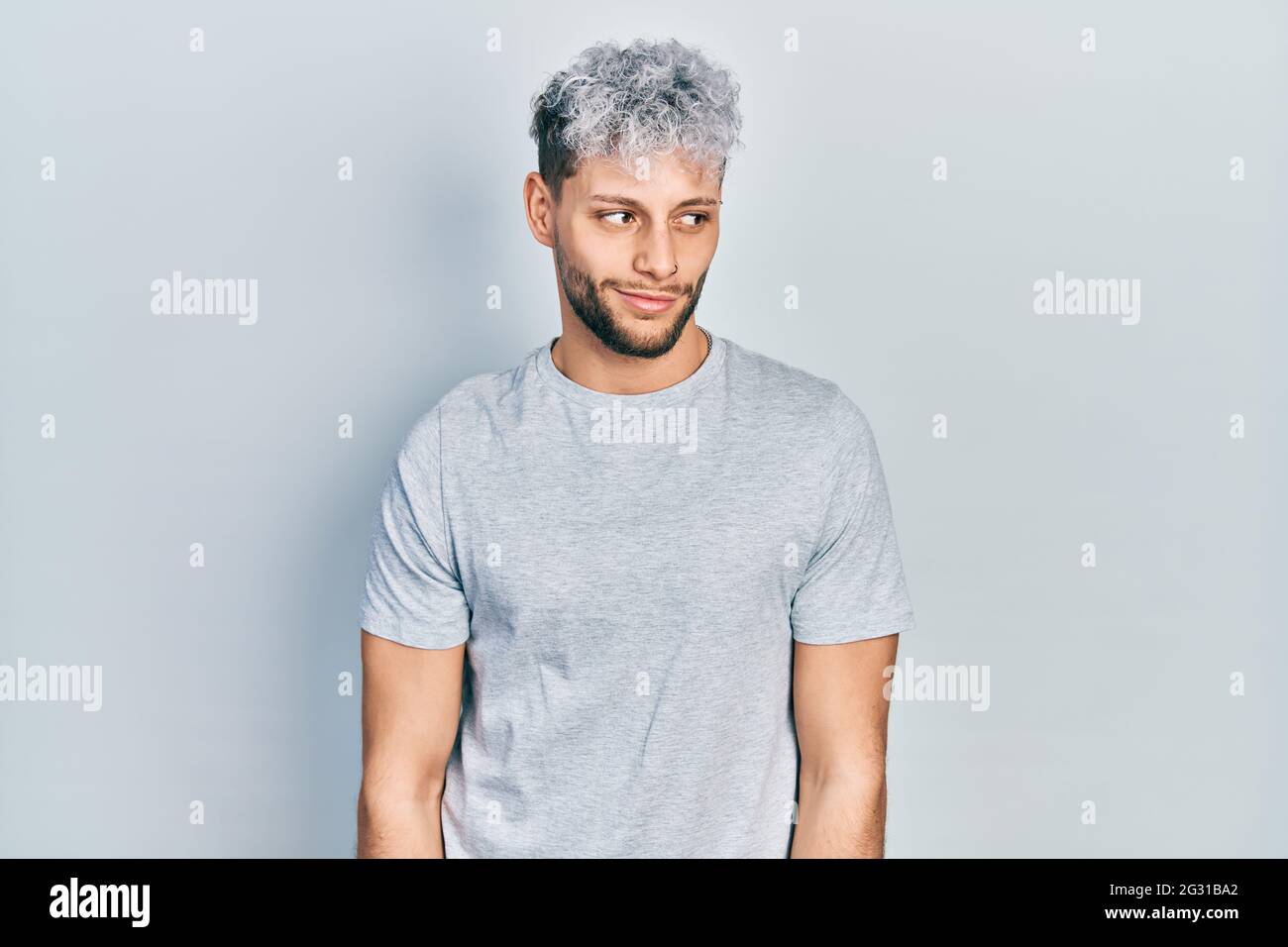 Joven hombre hispano con cabello teñido moderno con camiseta gris informal  sonriendo mirando hacia el lado y mirando hacia el lado mirando hacia el  lado Fotografía de stock - Alamy