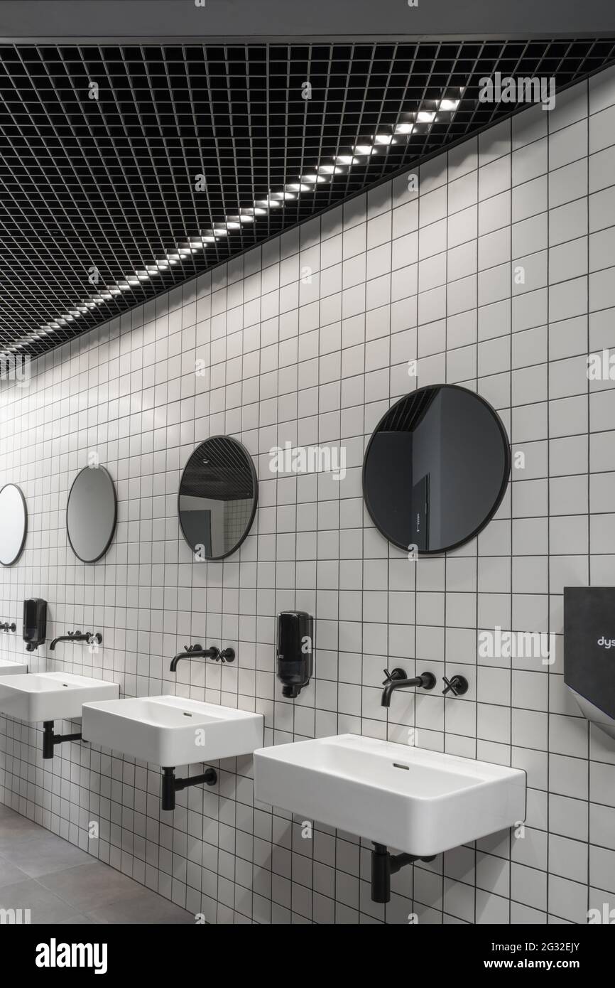 Moderno baño público interior mínimo con baldosas blancas estilo metro,  espejos redondos, techo negro Fotografía de stock - Alamy