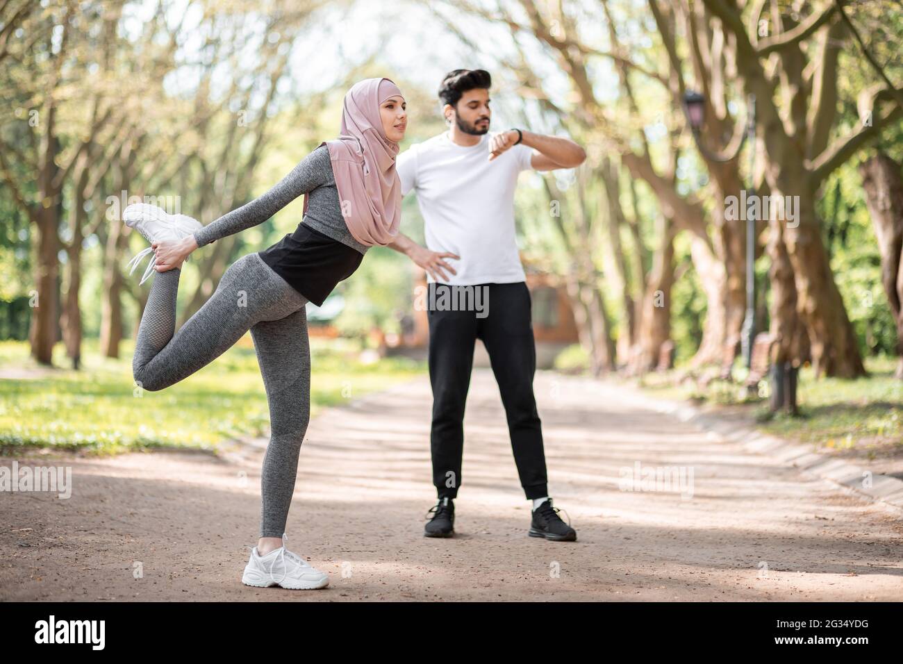 Mujer activa con ropa deportiva y piernas de hijab en el parque de verano.  Hombre árabe joven de pie sobre el fondo y con reloj inteligente.  Actividades deportivas al aire libre Fotografía