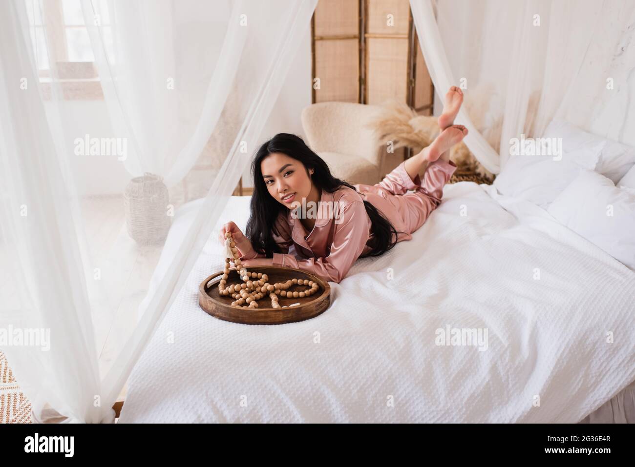 mujer asiática joven sonriente en pijama de seda tumbado en la cama y  tocando cuentas de madera en el dormitorio Fotografía de stock - Alamy