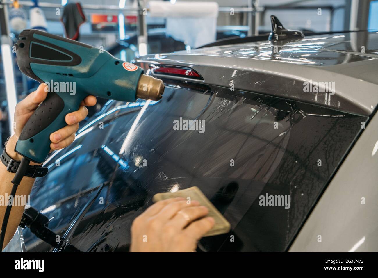 El dealer profesional calienta la película de tinte con el secador industrial para aplicar la tinción en el cristal del coche, cerca para arriba. Foto de stock