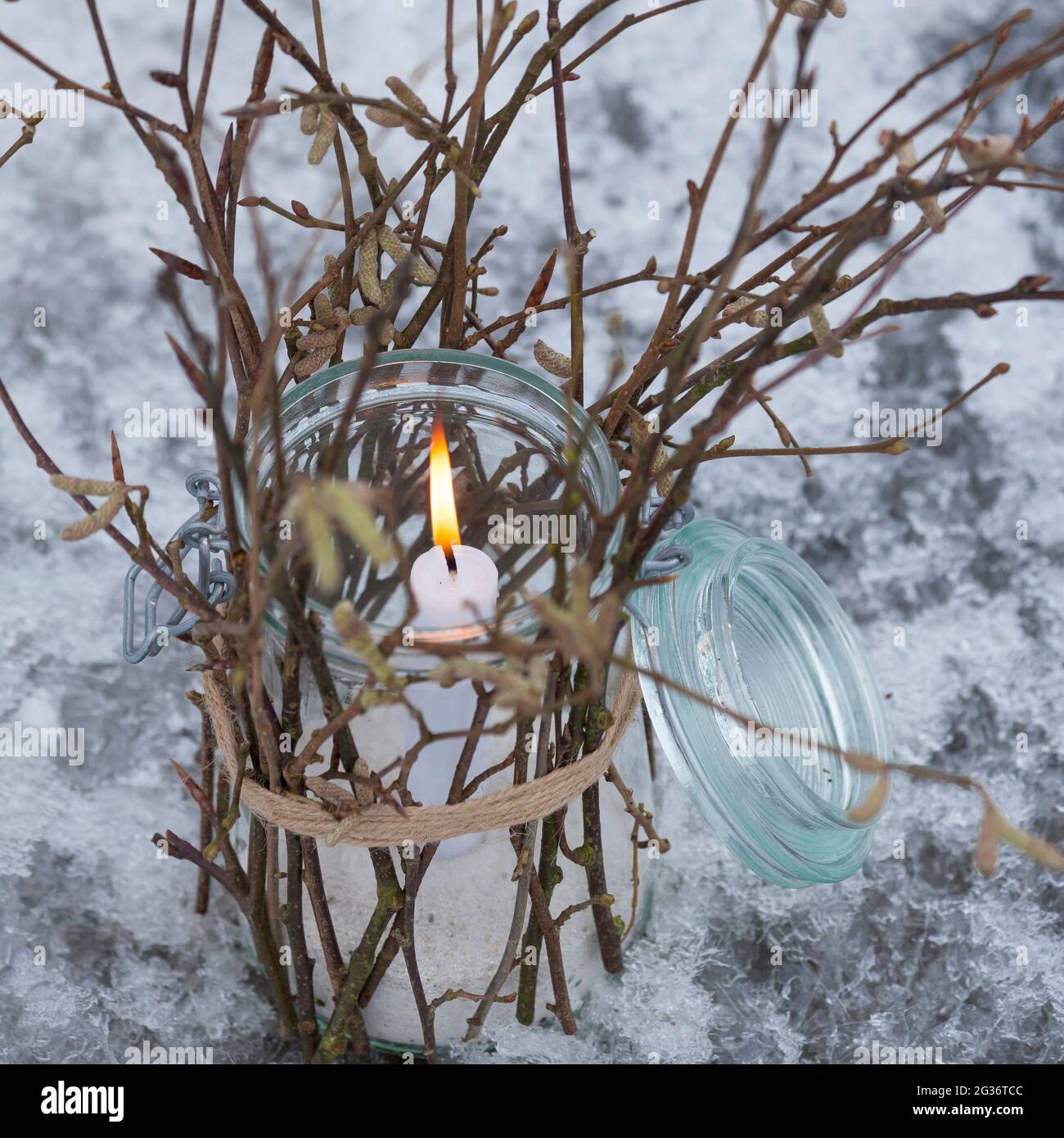 linterna, un cristal está decorado desde el exterior con palos, ramitas, ramitas. Una vela se levanta y quema en el vaso, protegido del viento, Foto de stock
