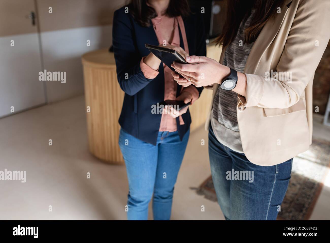 Sección media de dos mujeres caucásicas con ropa informal de pie, usando tableta, hablando Foto de stock