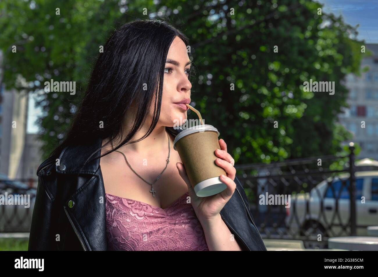 Mujer joven tomando café en la calle. Mujer en la calle de la ciudad bebiendo una bebida caliente. Imagen de una mujer joven atractiva que bebe café en la t Foto de stock