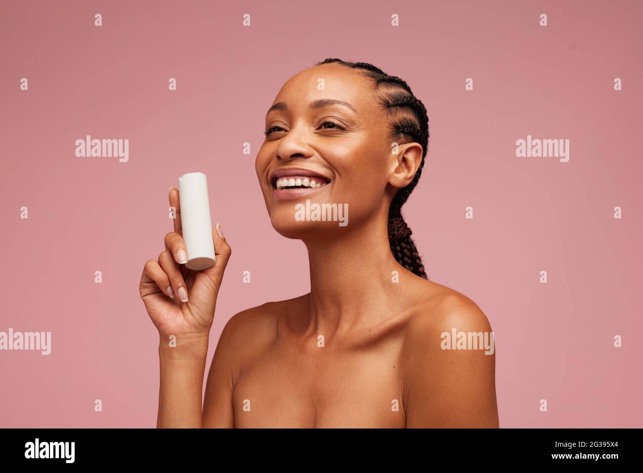 Buena mujer que sostiene el producto de la belleza. Mujer afroamericana que presenta crema cosmética sobre fondo rosa. Foto de stock
