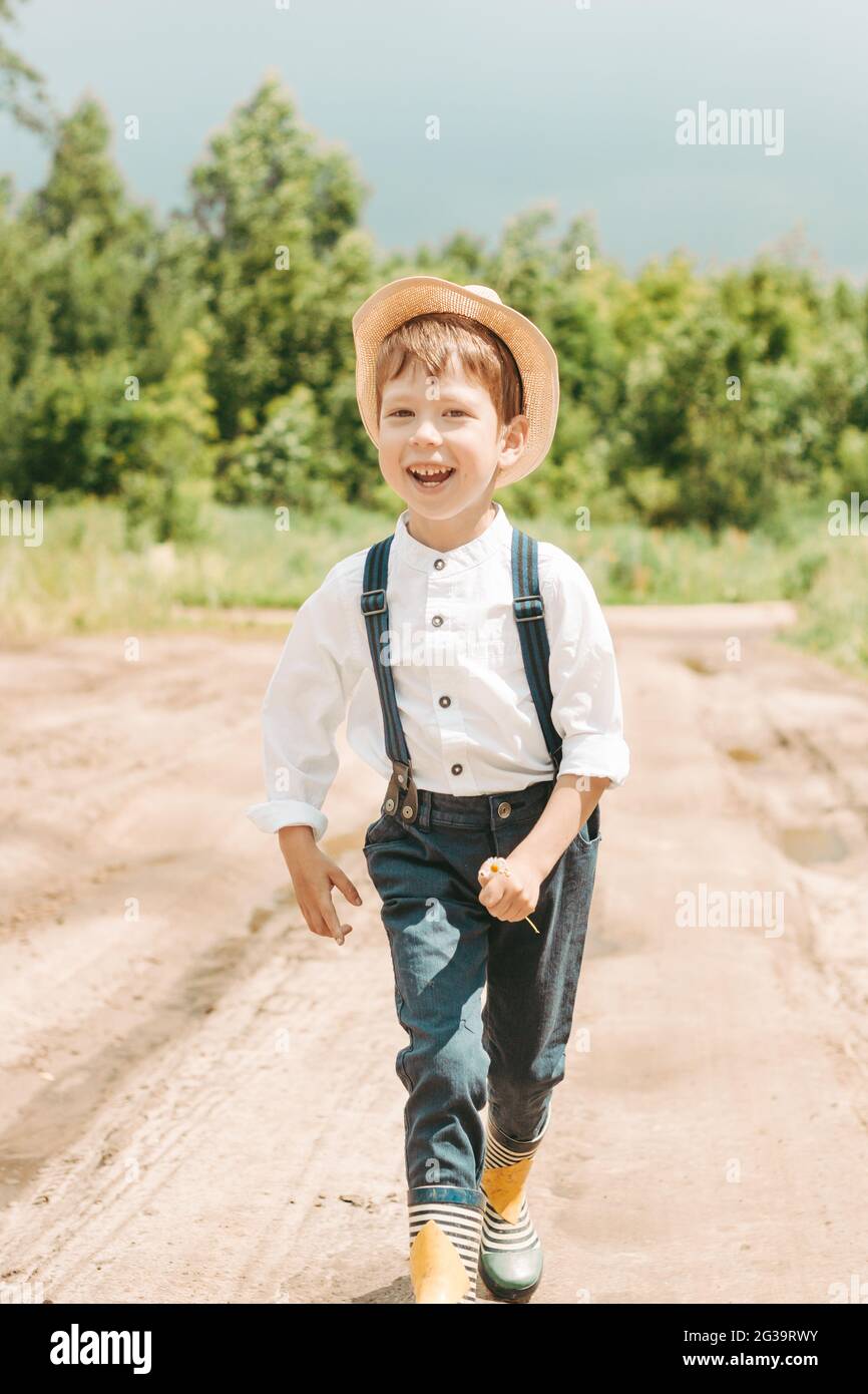 niño en un sombrero corre a través del campo. Pequeño granjero en un campo  de verano, niño pequeño feliz y lindo en un sombrero de paja. retrato de un  muchacho de pueblo.