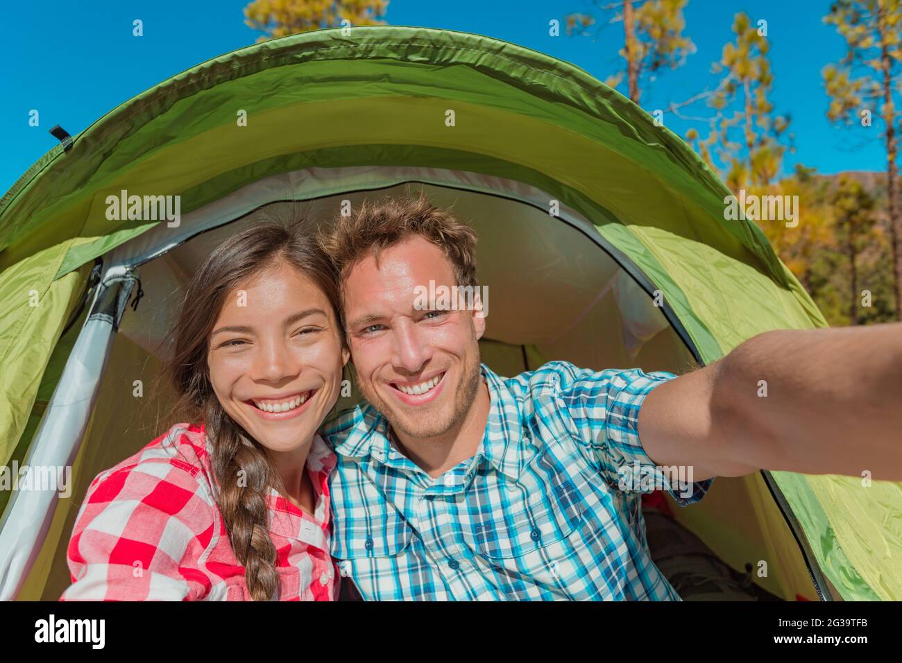 Pareja de turistas campistas tomando selfie en campamento de campaña en verano aventura viaje de vacaciones sonriendo a cámara. Se enfrenta a la mujer asiática autorretrato y. Foto de stock