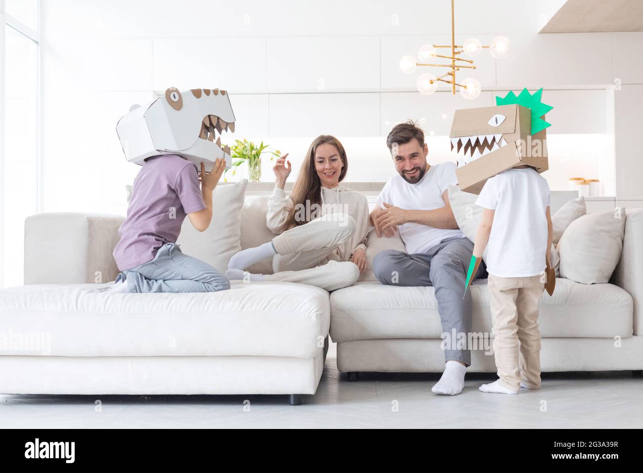 Feliz familia de padres y dos niños jugando dinosaurios en casa, niños usando una máscara de cartón hecha a mano Fotografía de stock - Alamy Feliz familia de padres y dos niños jugando dinosaurios en casa, niños usando una máscara de cartón hecha a mano Fotografía de stock - Alamy
