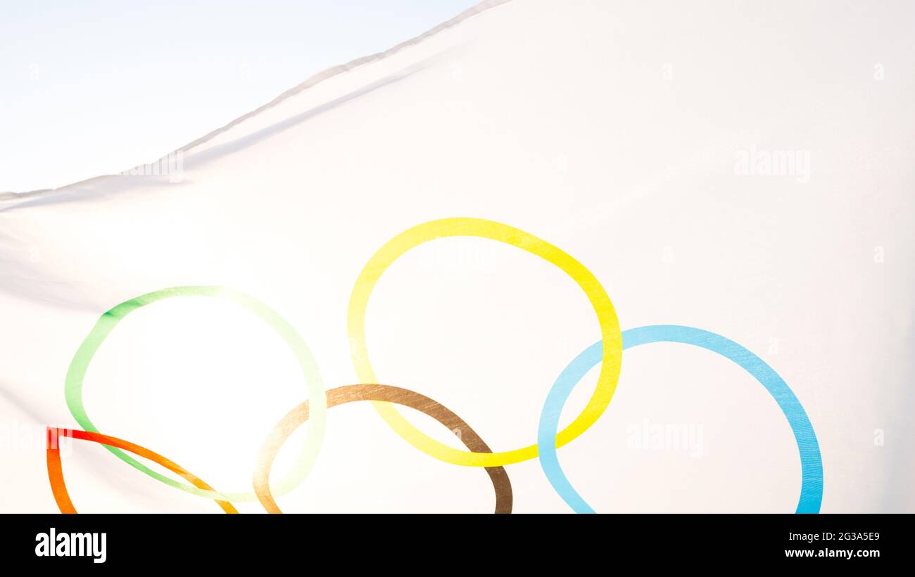 La bandera olímpica revolotea en el viento contra el fondo del cielo y el sol en primer plano. El símbolo de los Juegos Olímpicos de los Deportes, los aficionados de compe Foto de stock