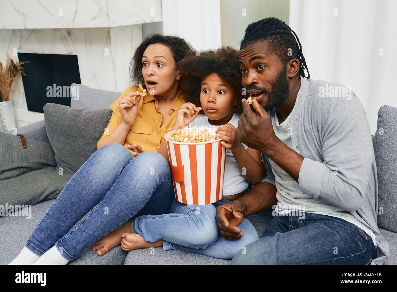 Padre, madre e hijo se sientan en un sofá con caras asustadas mientras ven  una película de miedo en el cine en casa Fotografía de stock - Alamy