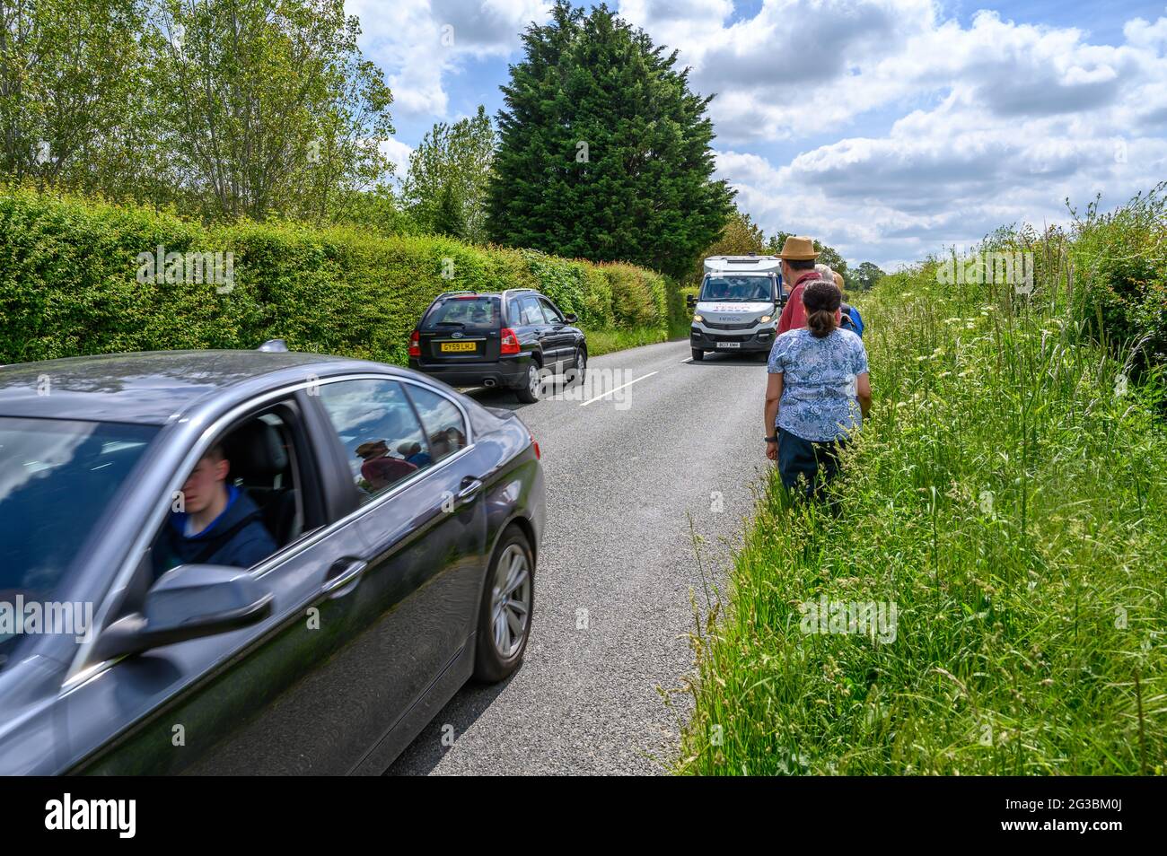 Un grupo de jugadores que se encuentran en el borde de la hierba mientras el tráfico pasa por South Road entre Plumpton Green y South Chailey, East Sussex, Engl Foto de stock