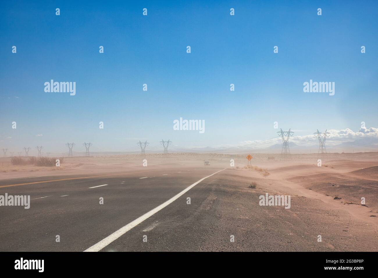 Pilones de electricidad y los cables que llevan cruzando una carretera en semi-desierto con una capa de polvo soplando a través de la carretera en Arizona, los Estados Unidos Foto de stock