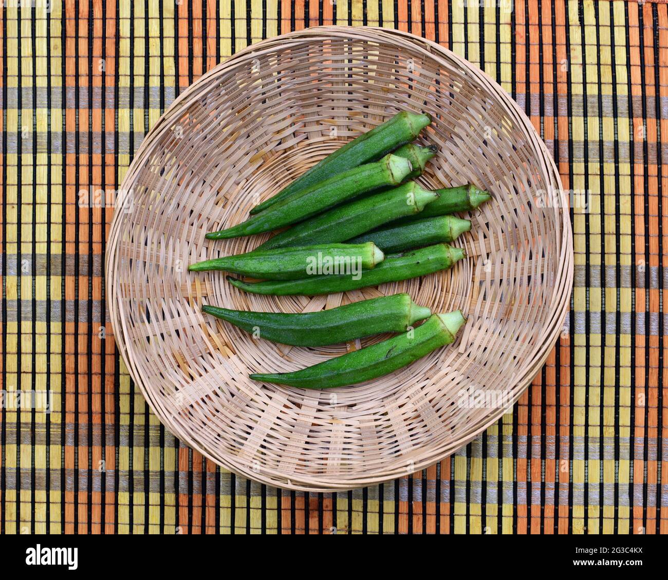 podas de okra verde en una pequeña cesta sobre una alfombra de paja de color Foto de stock