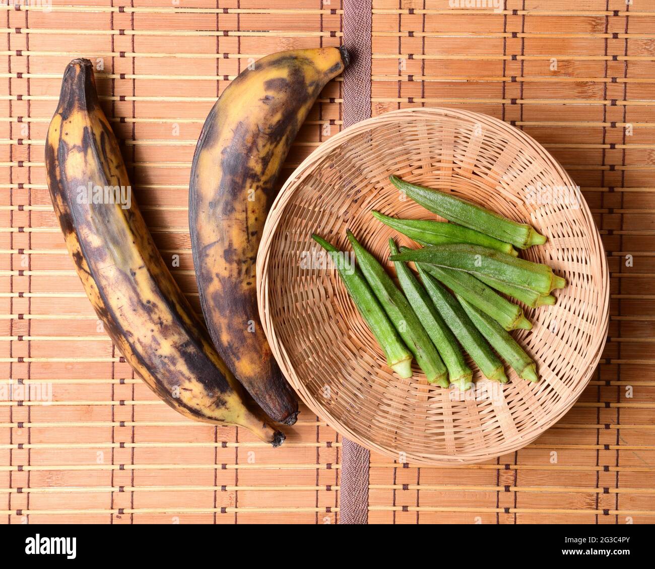 hortalizas tropicales okra y plátano maduro en una alfombra de bambú Foto de stock