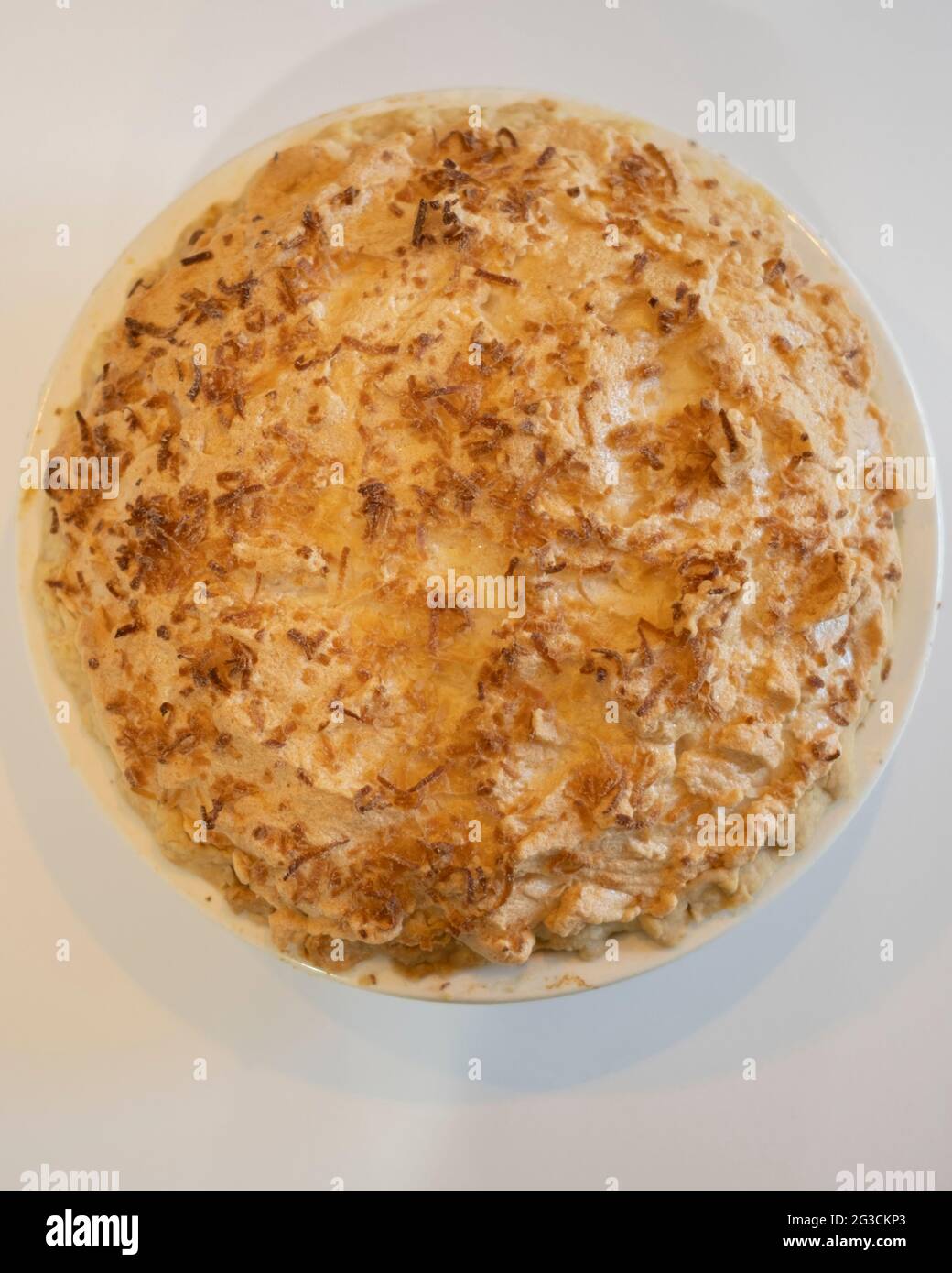 Una tarta de crema de merengue de coco dorado y horneada entera vista desde arriba sobre un fondo blanco. EE.UU Foto de stock