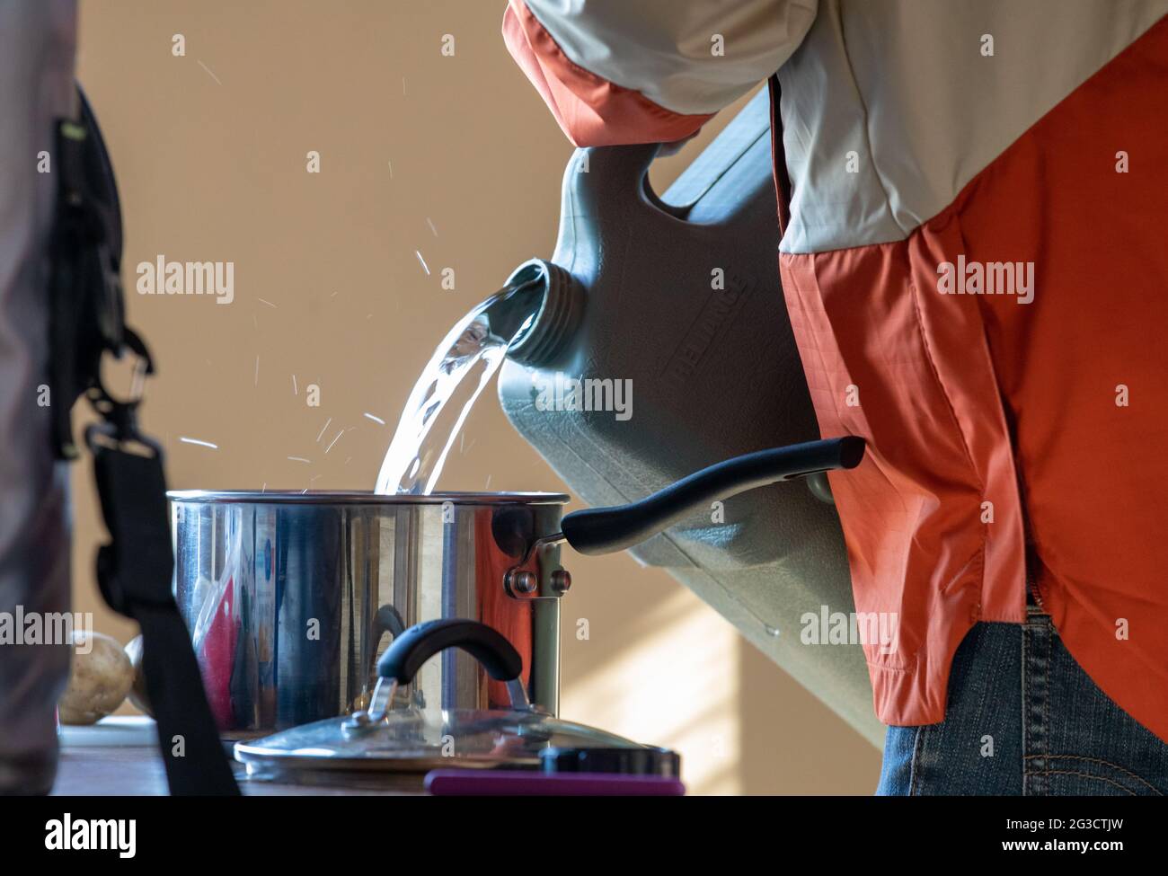 Hombre llenando una olla de metal con reserva de agua en un recipiente interior Foto de stock