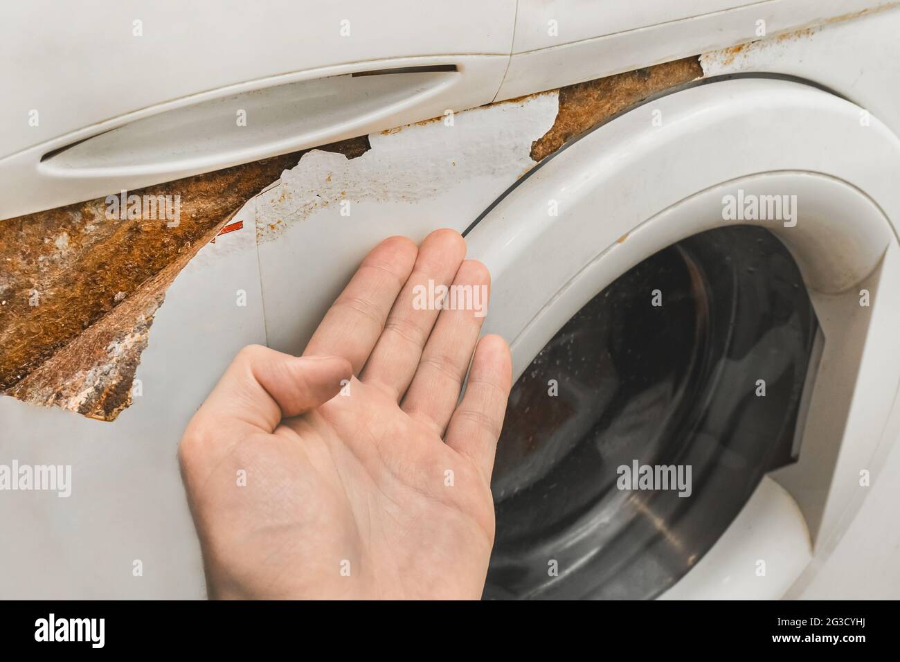La mano de un hombre apunta con los dedos a un rastro de óxido al lado del  teclado frontal de una lavadora vieja rota. Los electrodomésticos llevan el  concepto Fotografía de stock -