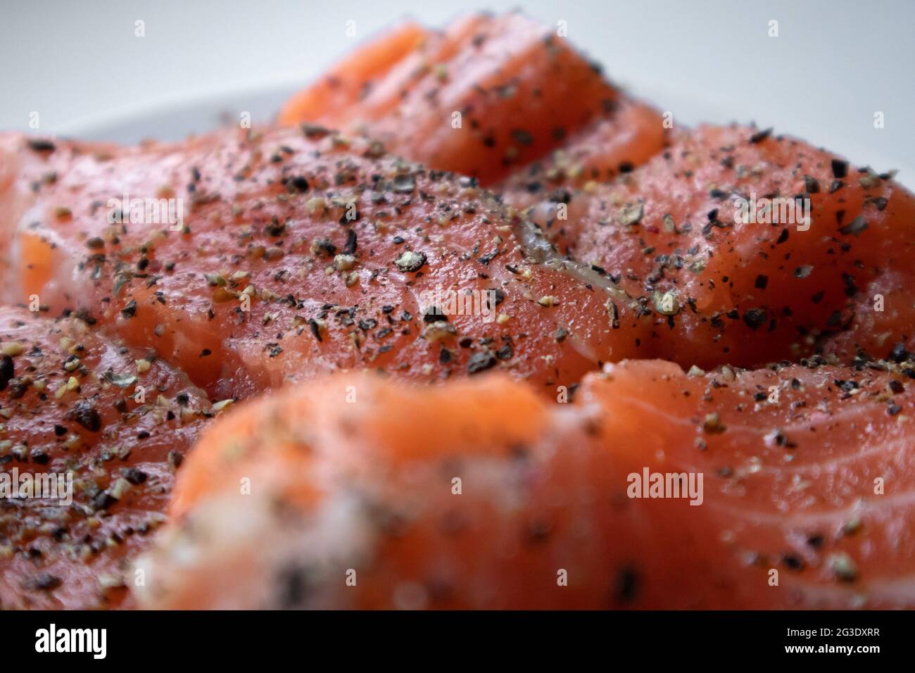 Apetitosos trozos de salmón crudo fresco con especias tumbadas un plato blanco Foto de stock