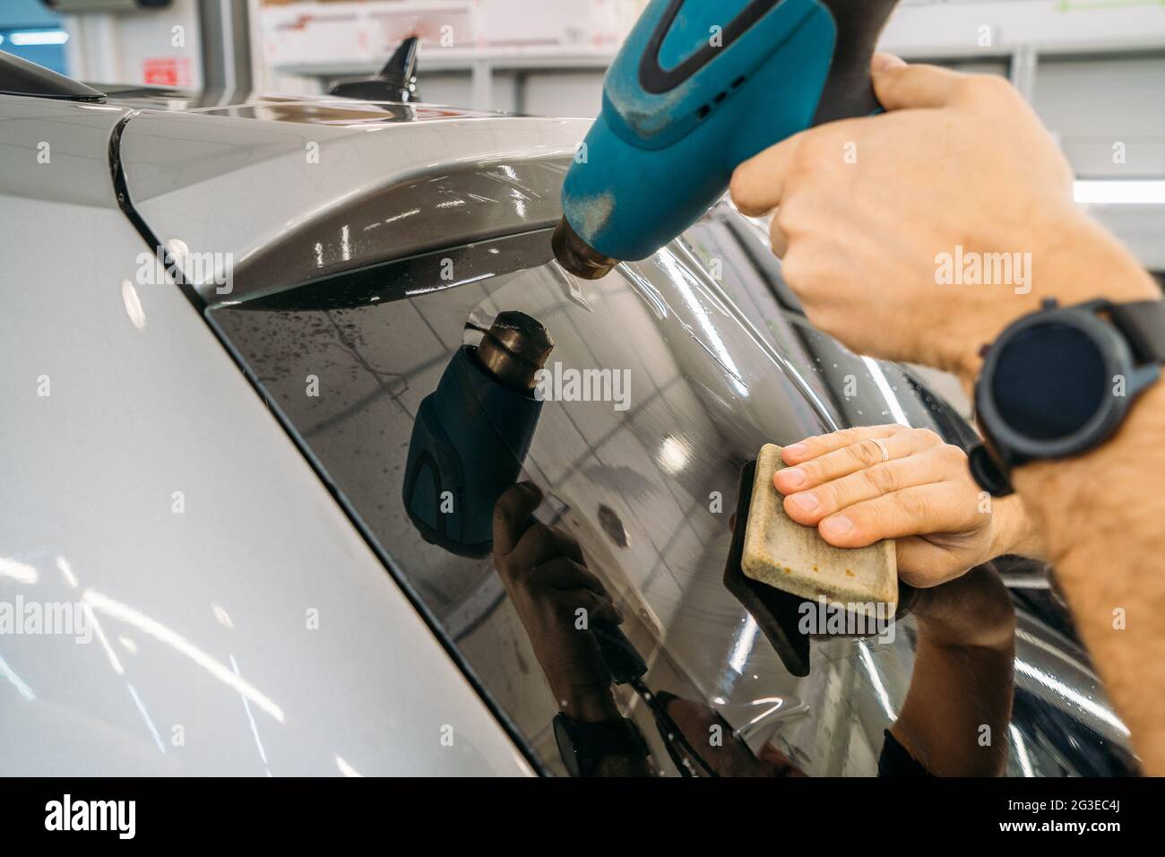 El dealer profesional calienta la película de tinte con el secador industrial para aplicar la tinción en el cristal del coche, cerca para arriba. Foto de stock