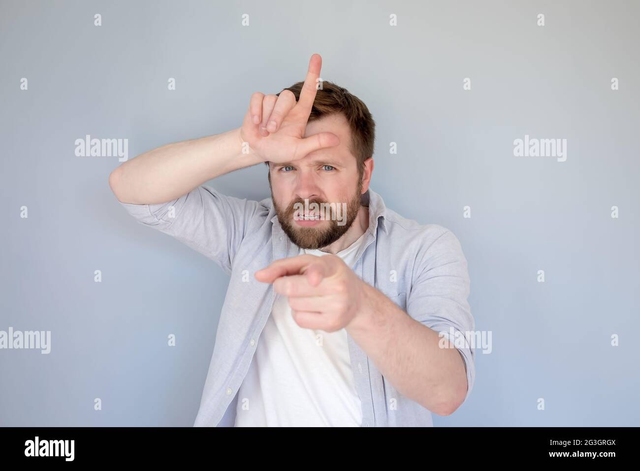 Un hombre caucásico molesto con ropa casual insulta a alguien con un gesto perdedor, dedos en la frente y viciosamente apunta al dedo índice. Foto de stock