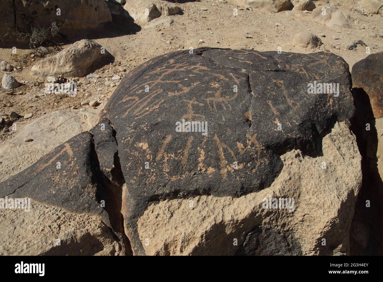 Antiguas tallas de roca de jinetes de camellos con lanzas, letras griegas y formas abstractas en la Patina de una roca de piedra caliza en Nachal Zin, el desierto de Negev Foto de stock