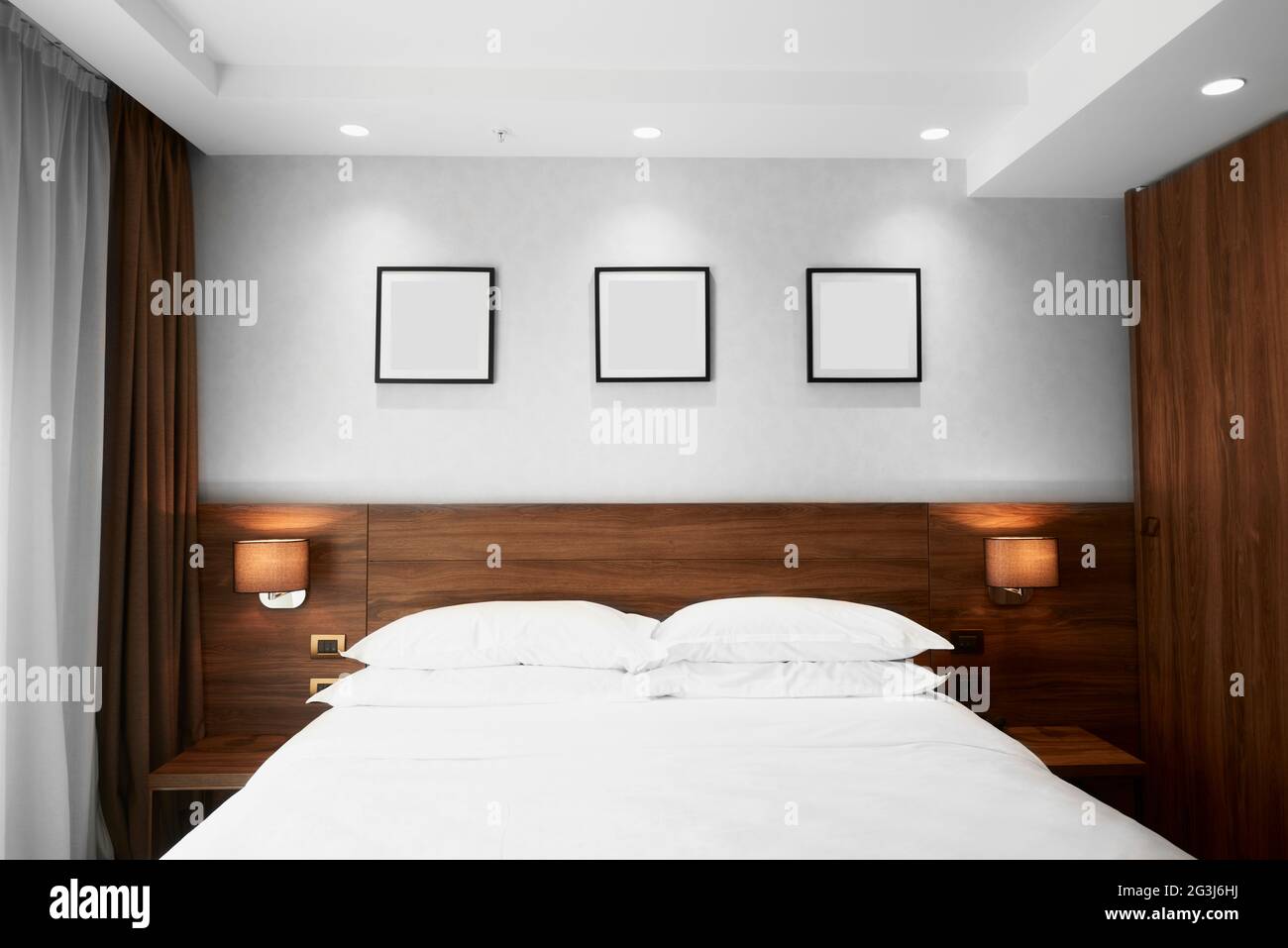 Lujosa habitación con cama tamaño king y tres fotografías en blanco en la pared Foto de stock