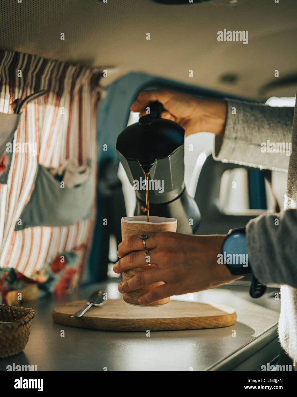 Persona que sirve café desde una cafetera italiana a una taza en una furgoneta en un tono de color café clásico Foto de stock