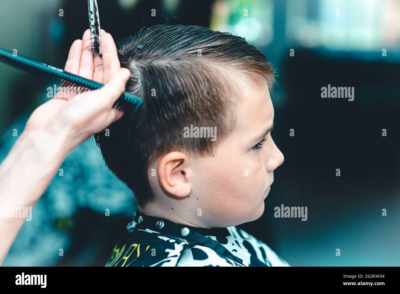 Corte de pelo para un niño pequeño en un salón de belleza. Mano con el  instrumento utilizado para cortar las manos de hair.Peluquería sosteniendo  un peine y un tijera.CL colorido Fotografía de