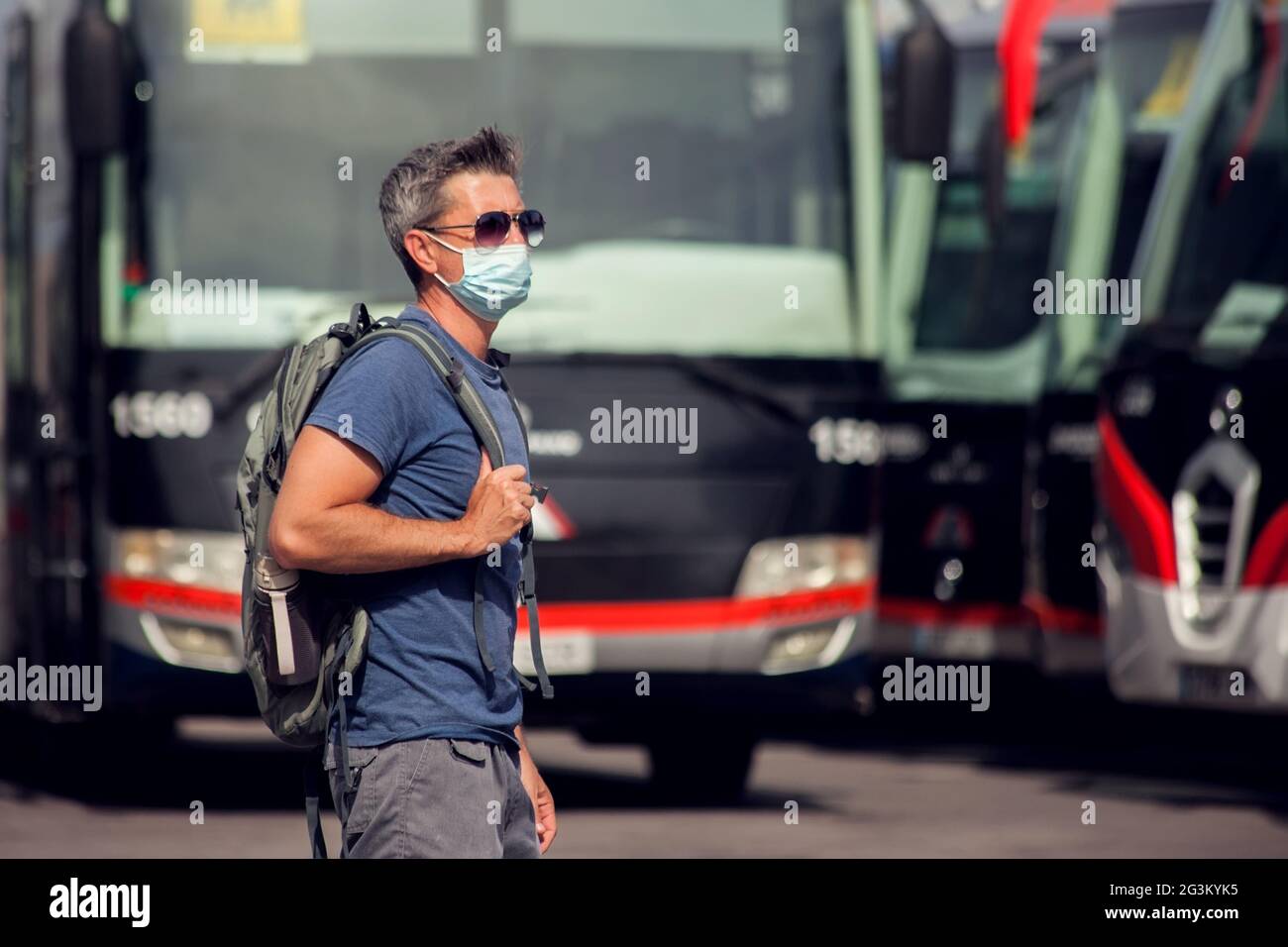 Viajero en la estación de autobuses al aire libre. Hombre con mochila y máscara médica esperando un autobús. Concepto de viajes y turismo Foto de stock
