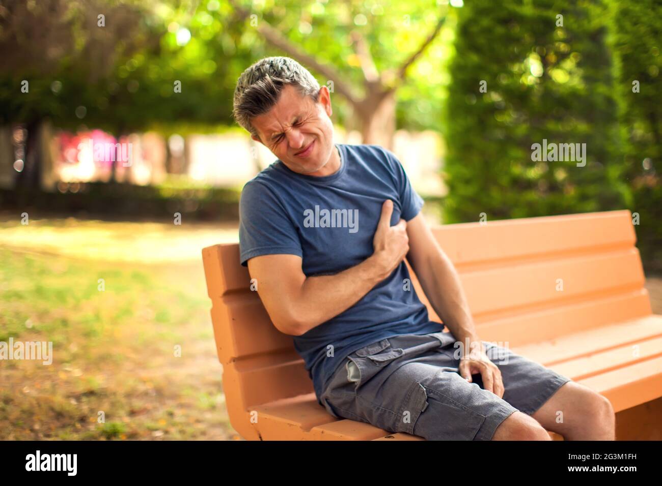 Hombre con dolor de corazón al aire libre. Hombre sintiendo dolor en el pecho sentado en el banco en el parque. Concepto de salud y medicina Foto de stock