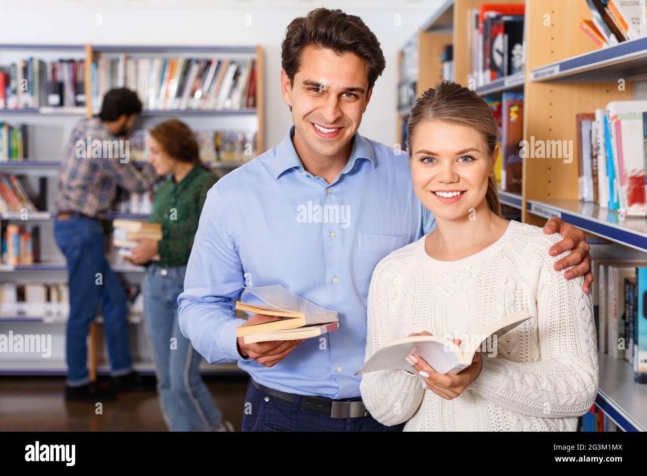 Guapo joven y atractiva chica elegir libros juntos en la biblioteca de la universidad Foto de stock