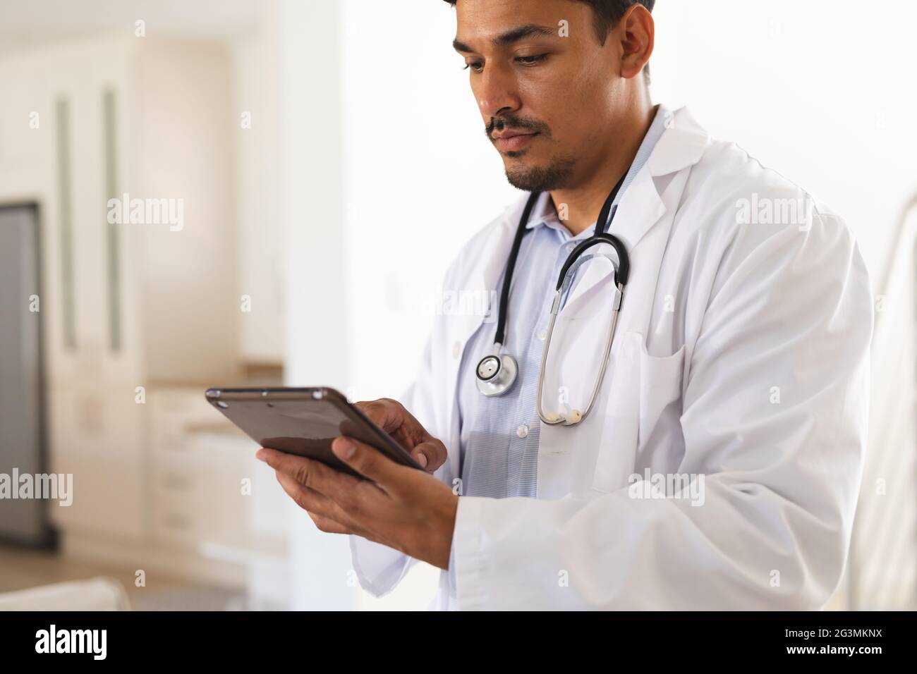 Doctor hispano en bata de laboratorio concentrándose usando tableta digital Foto de stock