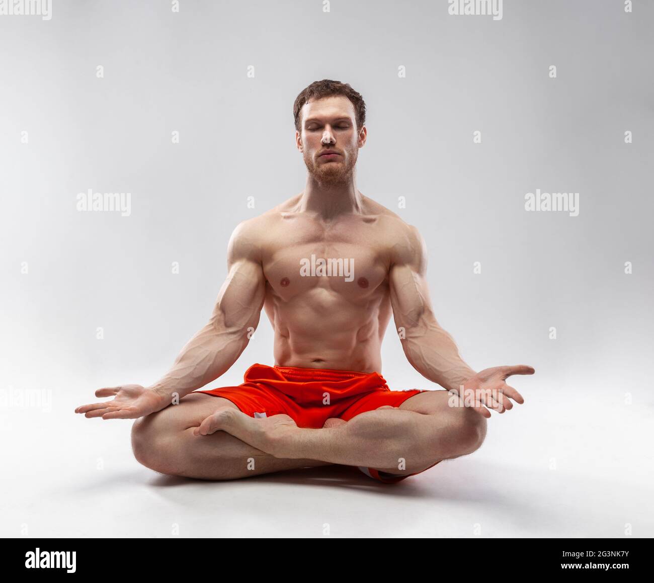 Un hombre con sus ojos cerrados y el cuerpo musculoso sentado en la postura del loto Foto de stock