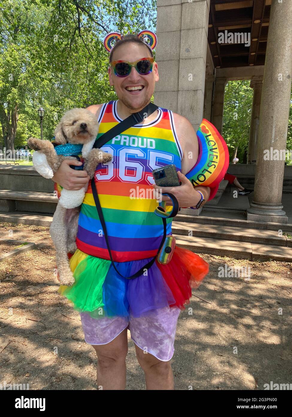 Hombre gay con su pooch durante el mes de orgullo gay en su camino con otros dueños de mascotas al estanque de perros en Prospect Park en un día caluroso junio