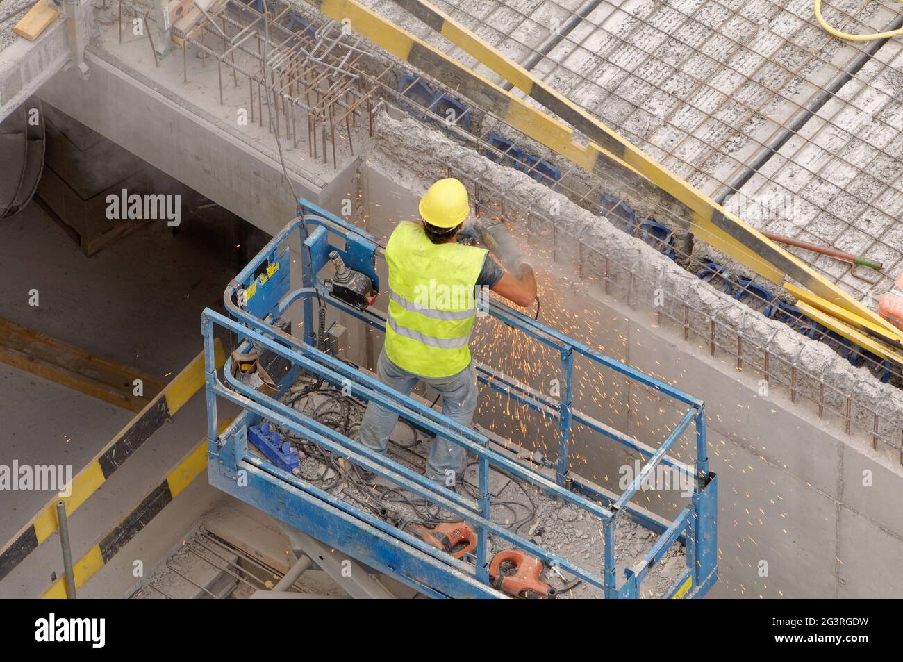 Trabajador en ascensor usando una muela en un lugar de construcción (edificio) protegido por un casco Foto de stock