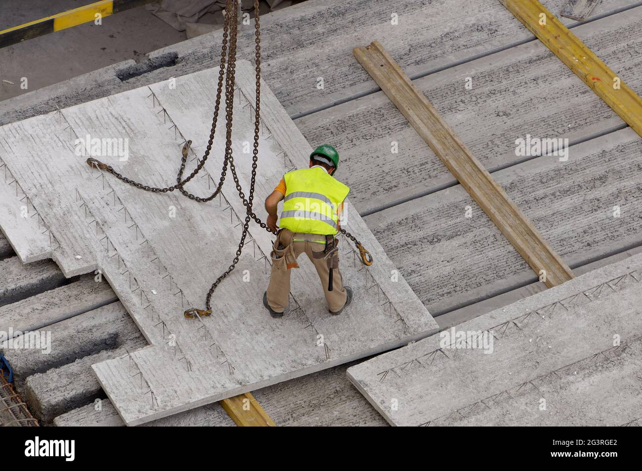 El trabajador está hunhgancho cadenas y ganchos de la losa de hormigón en un sitio de construcción de un edificio Foto de stock