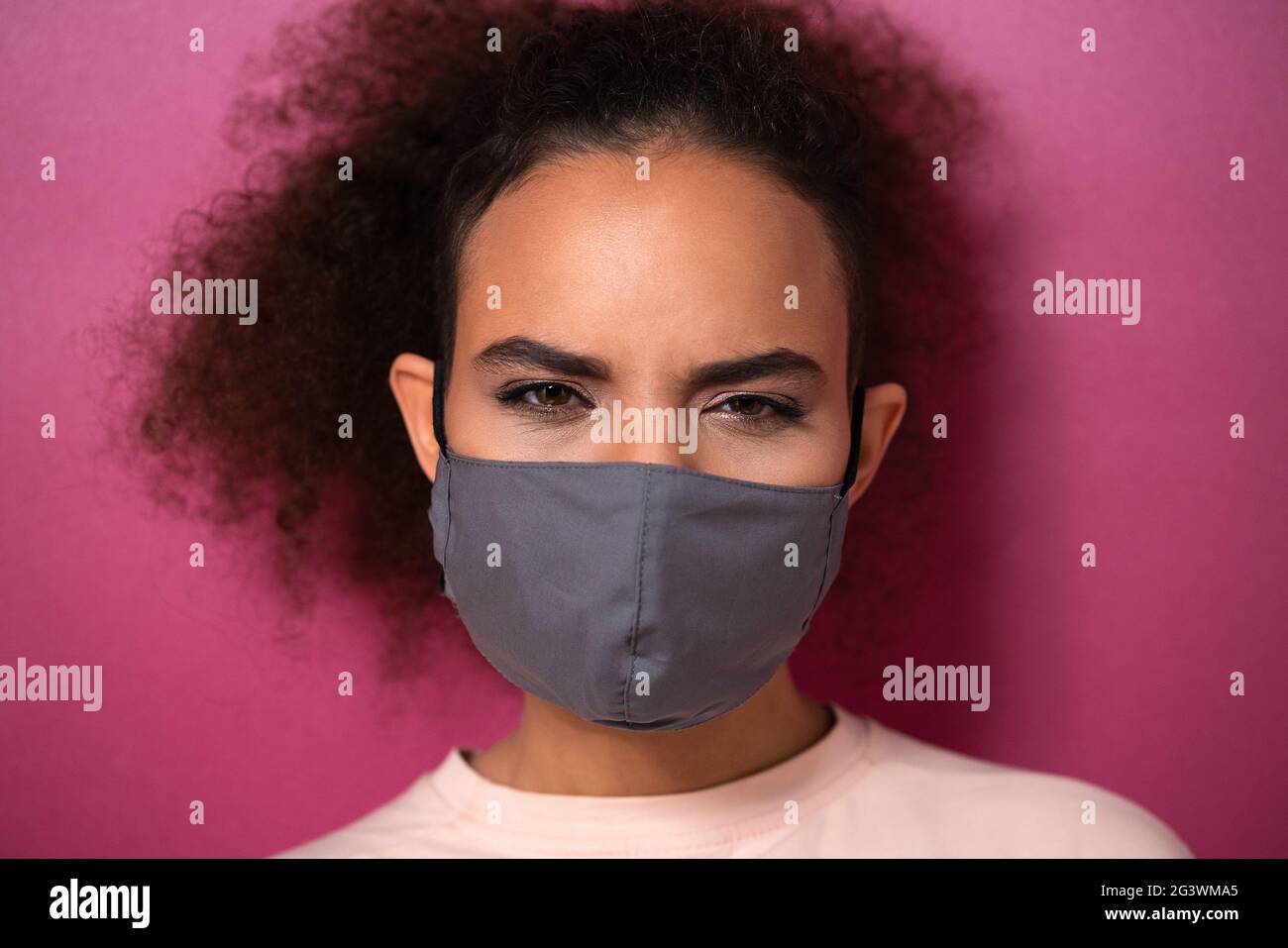 Cuestionar o estudiar mirar usando máscara facial reutilizable afroamericana encantadora chica en peachy camiseta, para evitar que otros Foto de stock
