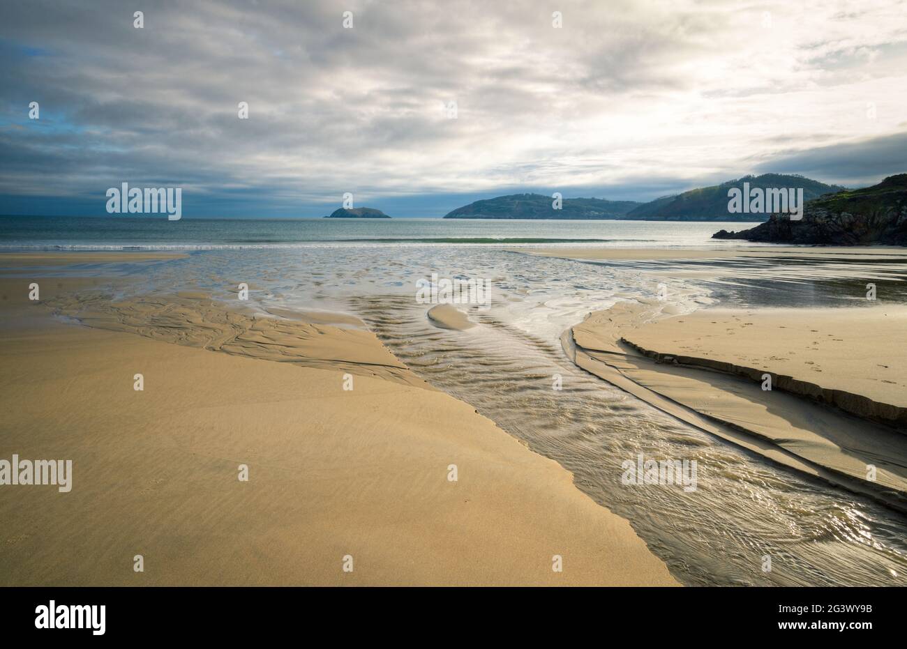 En una playa de arenas doradas, un arroyo de agua dulce entra en el océano en Ortigueira Galicia Foto de stock