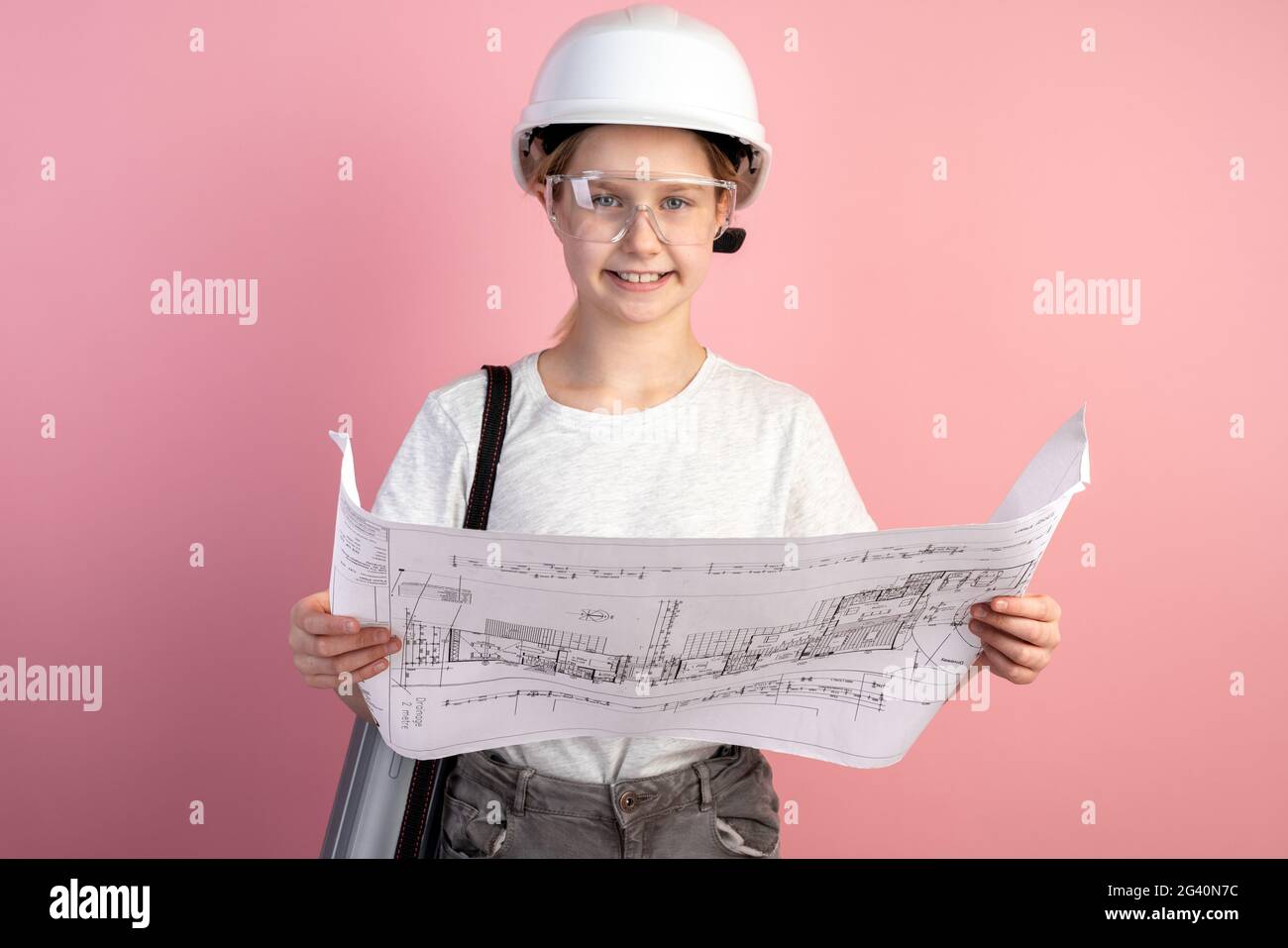 Linda niña en un casco de construcción sobre un fondo rosa. Adolescente  sosteniendo un dibujo en sus manos Fotografía de stock - Alamy
