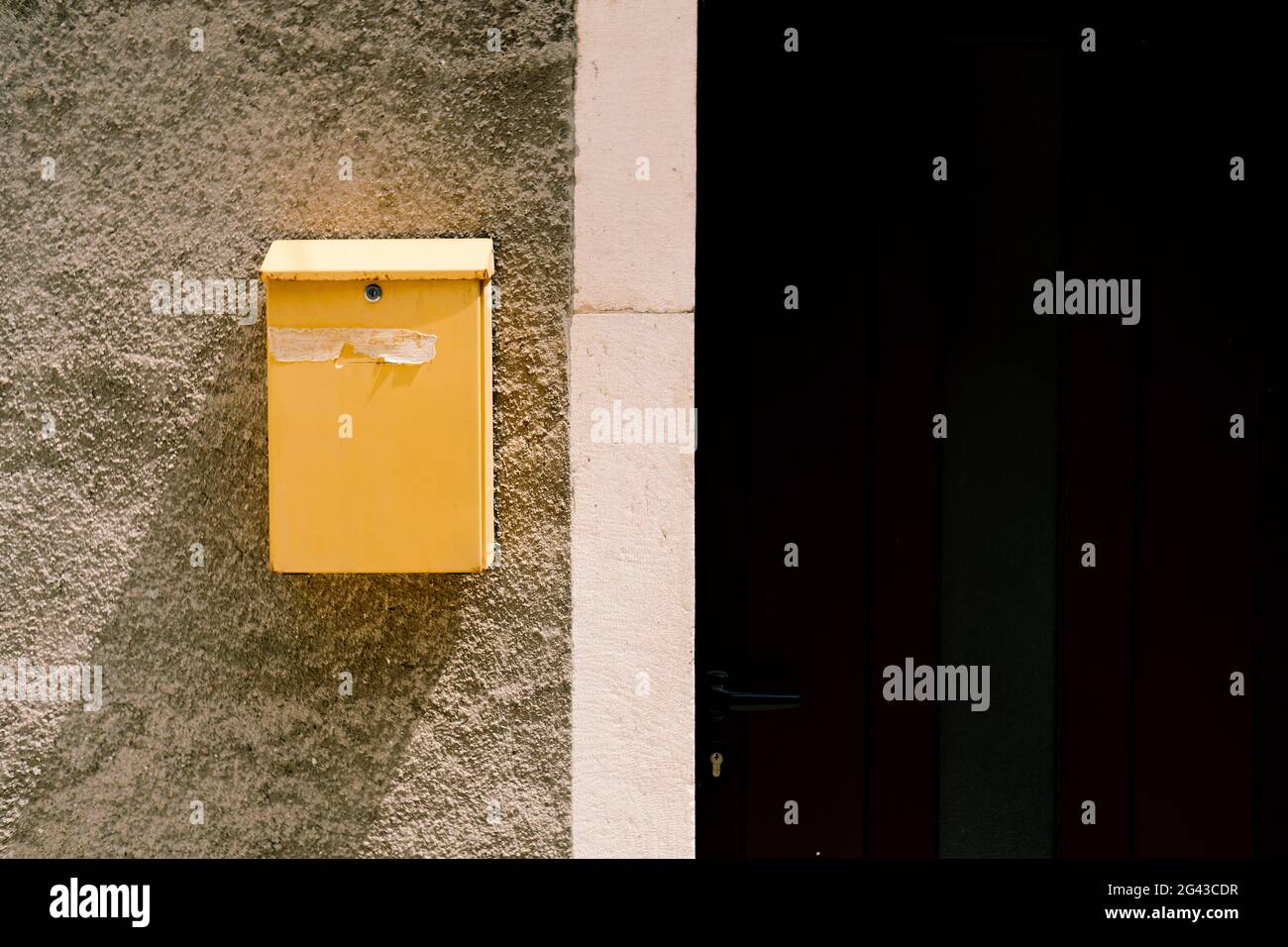 Un buzón amarillo en un día soleado en una pared de piedra cerca de la puerta de la casa. Foto de stock