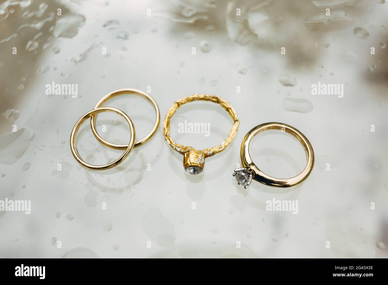 Primer plano de anillos de boda de oro, un anillo de compromiso y un anillo  de aluminio sobre un fondo gris en gotas de lluvia Fotografía de stock -  Alamy