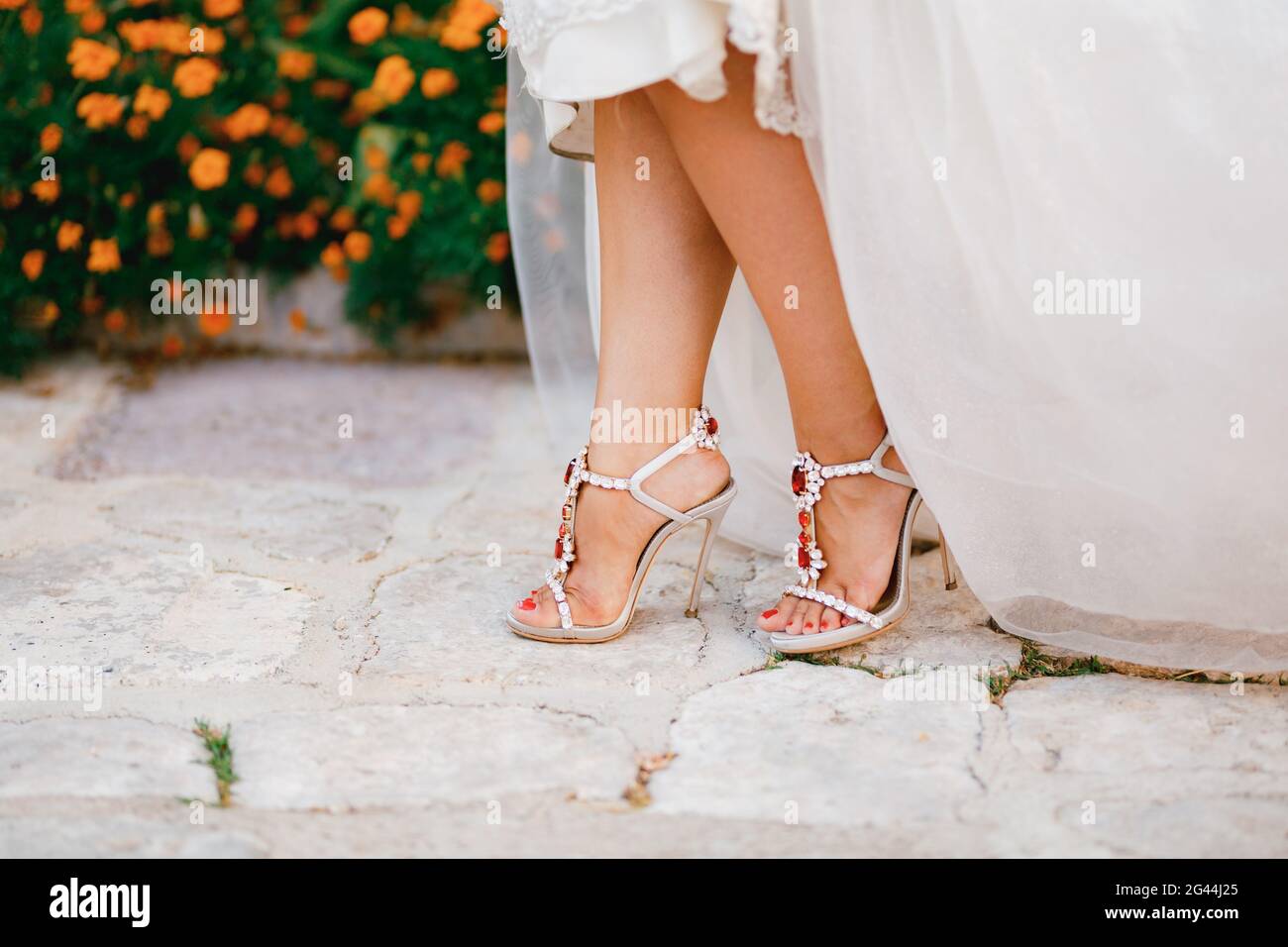 Piernas para novia en sandalias con estilo con cristales con tacones altos  que se echan por debajo del vestido de boda, primer plano Fotografía de  stock - Alamy