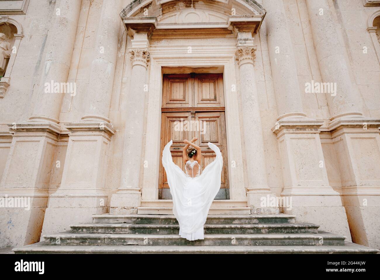 La novia tiró sus brazos sobre su cabeza, la falda se aletea alrededor de ella en las antiguas escaleras del templo en Prcanj Foto de stock