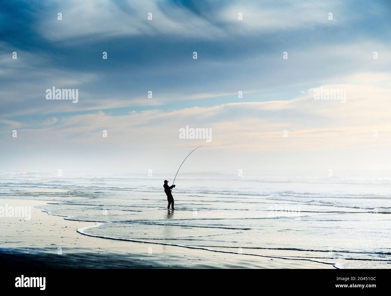 Silueta de pescadores pescando en la playa bajo el cielo azul Foto de stock