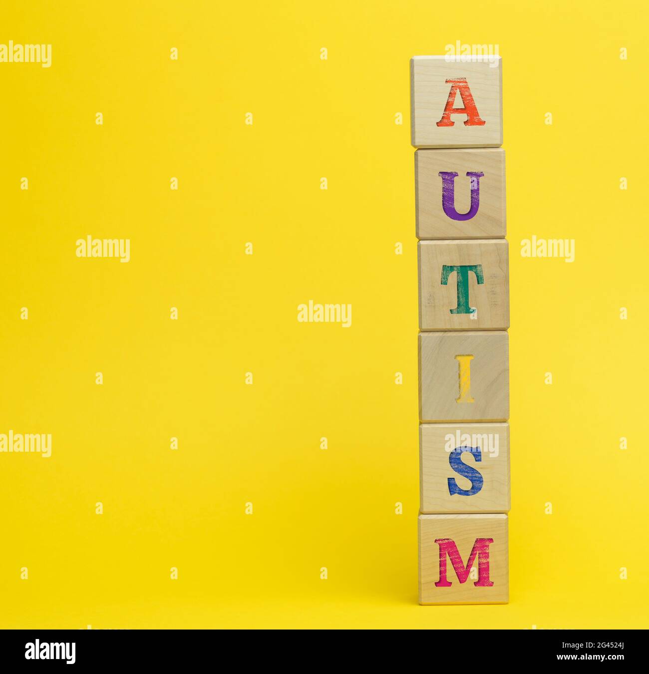 Cubos de madera con la inscripción autismo sobre fondo amarillo. Concepto de apoyo y estímulo para niños con desarrollo Foto de stock