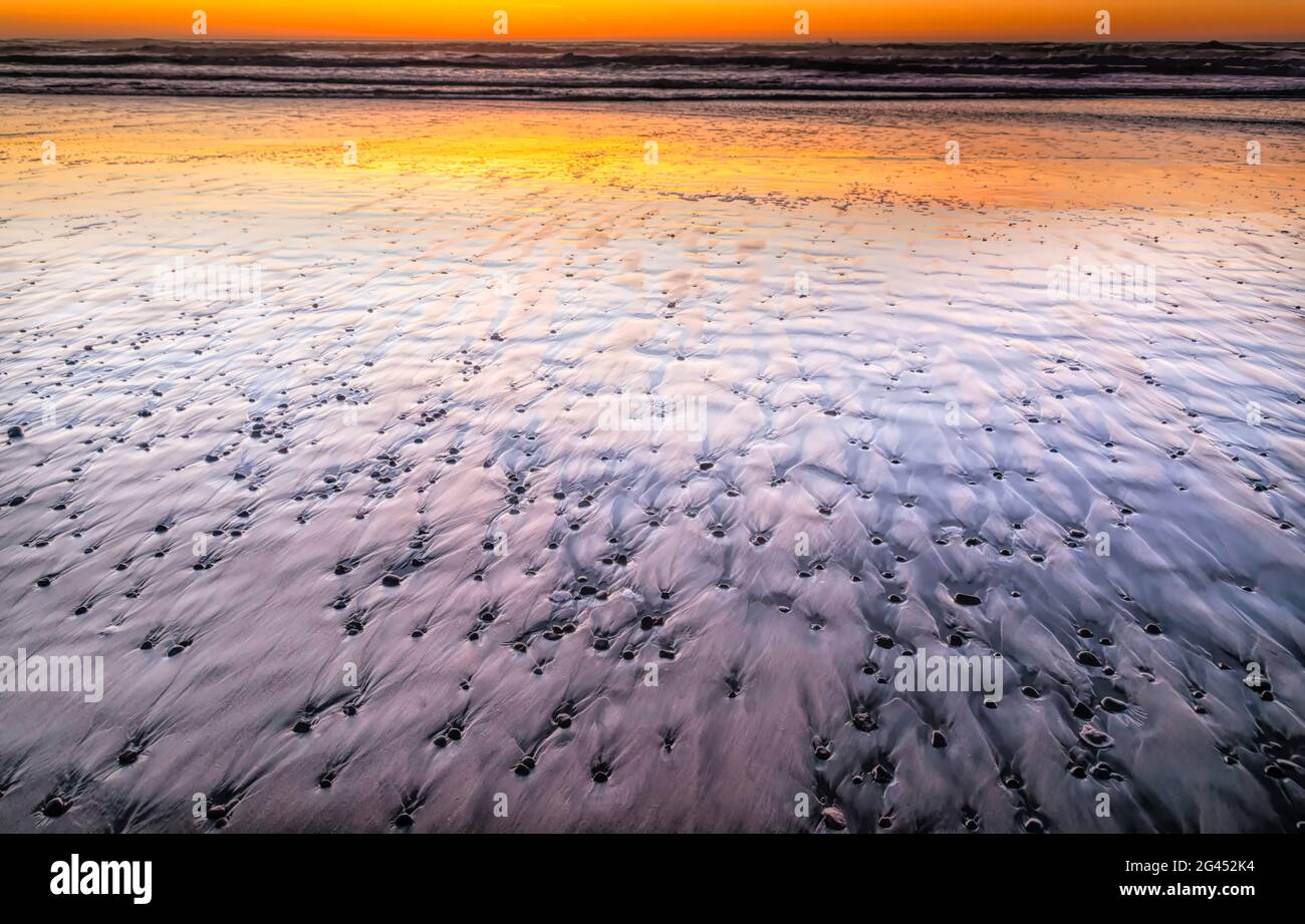 Guijarros en arena en la playa del Océano Pacífico al atardecer Foto de stock