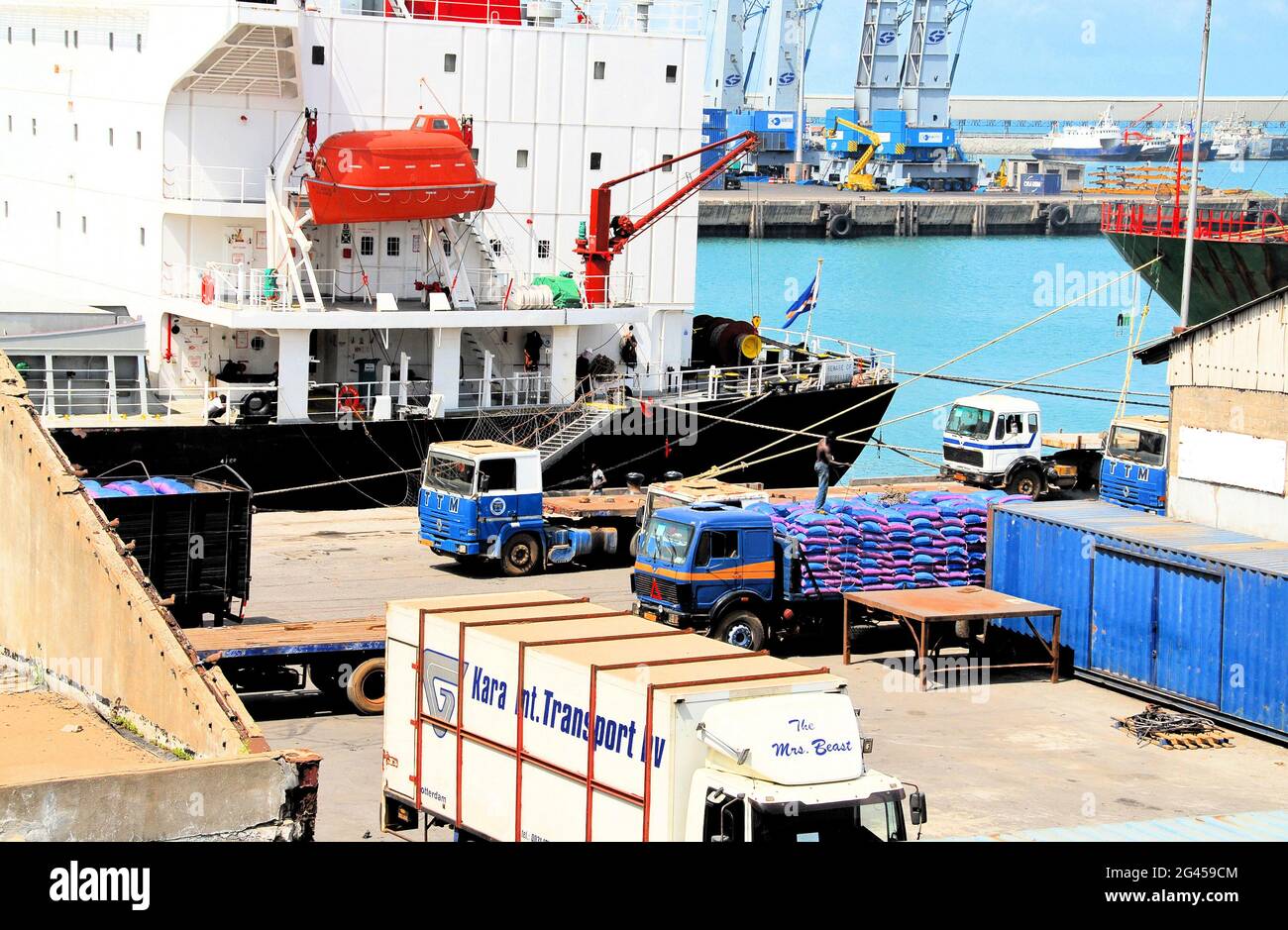 Descargando un barco en el Puerto de Lomé, Togo, mientras un hombre carga un camión con sacos de mercancías recién llegadas y otros camiones esperan su turno. Foto de stock