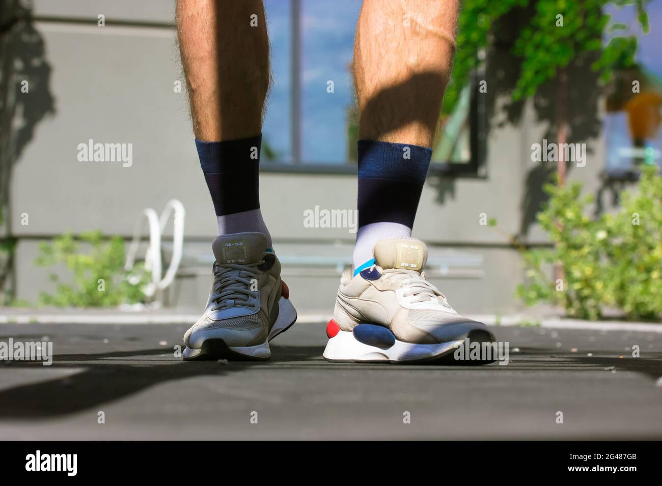 Un tipo con piernas musculares en sneakers grises y calcetines altos en un  terreno deportivo. Un hombre trabaja, calentándose antes de correr afuera  en un soleado día de verano. C Fotografía de