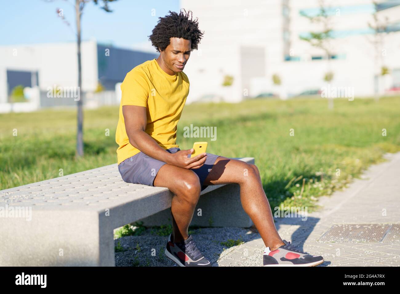 Hombre negro consultando su smartphone con alguna aplicación de ejercicio mientras descansa de su entrenamiento. Foto de stock