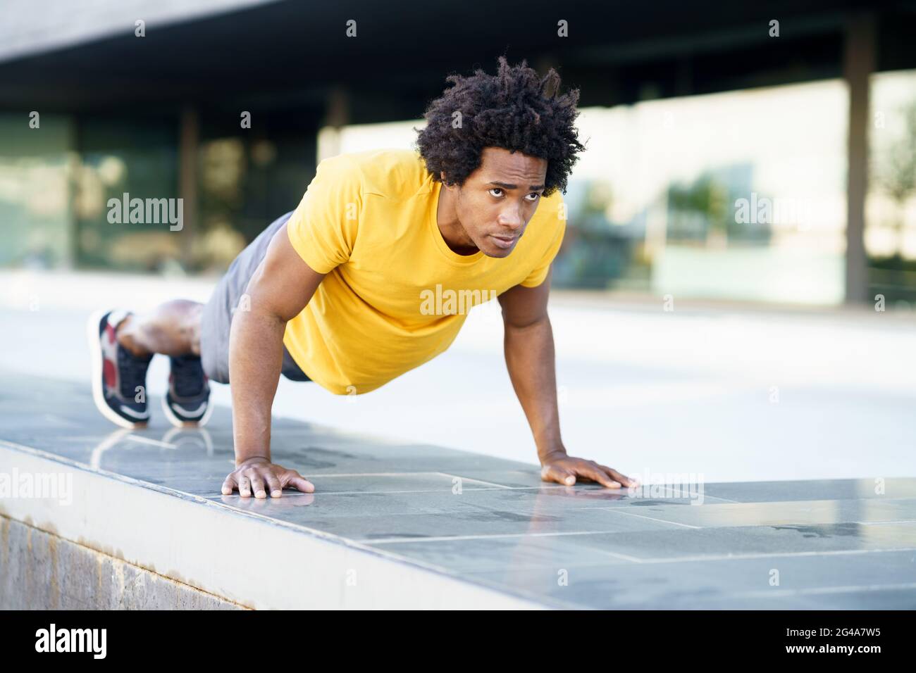 Hombre negro haciendo ejercicio de la inmersión del tríceps en banco de la calle de la ciudad. Foto de stock